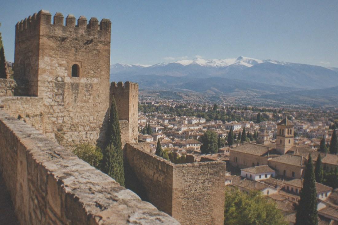 The Alcazaba fortress ramparts of the Alhambra with views over Granada's rooftops toward the Sierra Nevada.