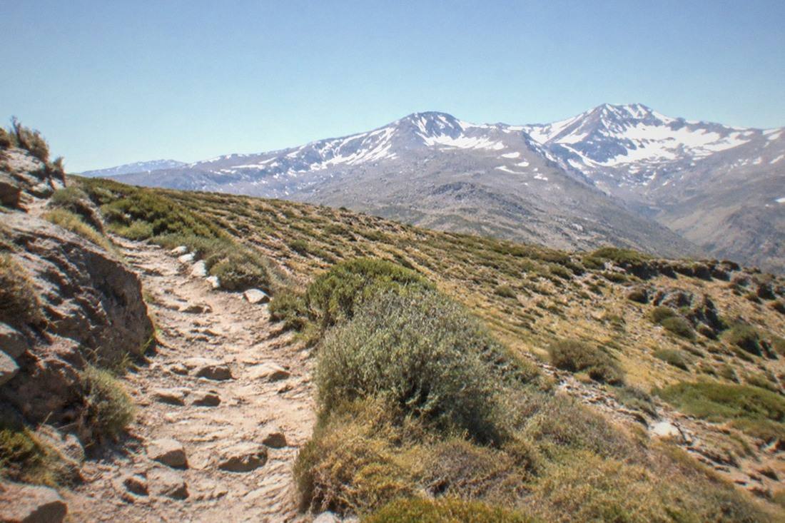 A rocky hiking trail through the Sierra Nevada mountains near Granada, snow-capped peaks in the distance.