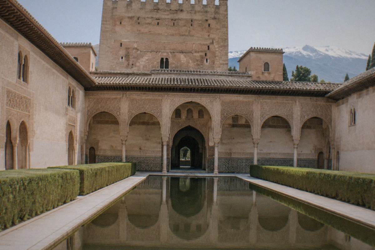 Carved stucco archways and a still reflecting pool in a Nasrid palace courtyard within the Alhambra.