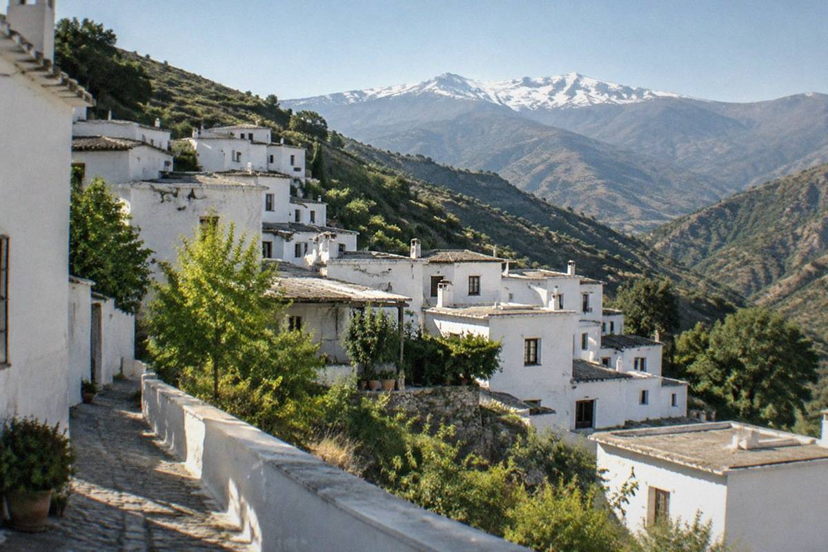 Whitewashed Alpujarras village houses with flat roofs terraced into a green mountainside near Granada.