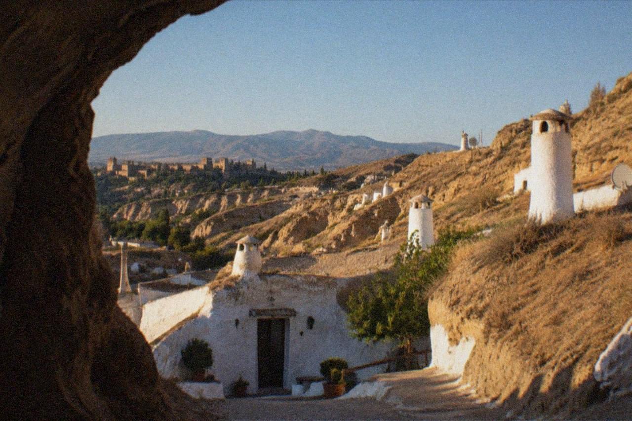 White cave houses built into the hillside of the Sacromonte district at dusk, with the Alhambra visible across the valley