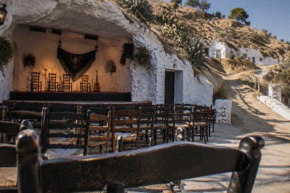 A small flamenco performance space inside a whitewashed Sacromonte cave with rows of chairs facing a low stage