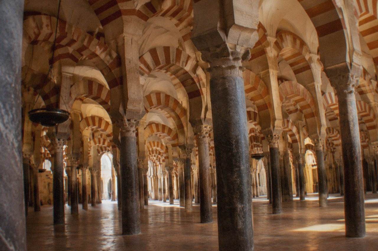 The bell tower and arched walls of the Mosque-Cathedral of Cordoba seen across a sunny square