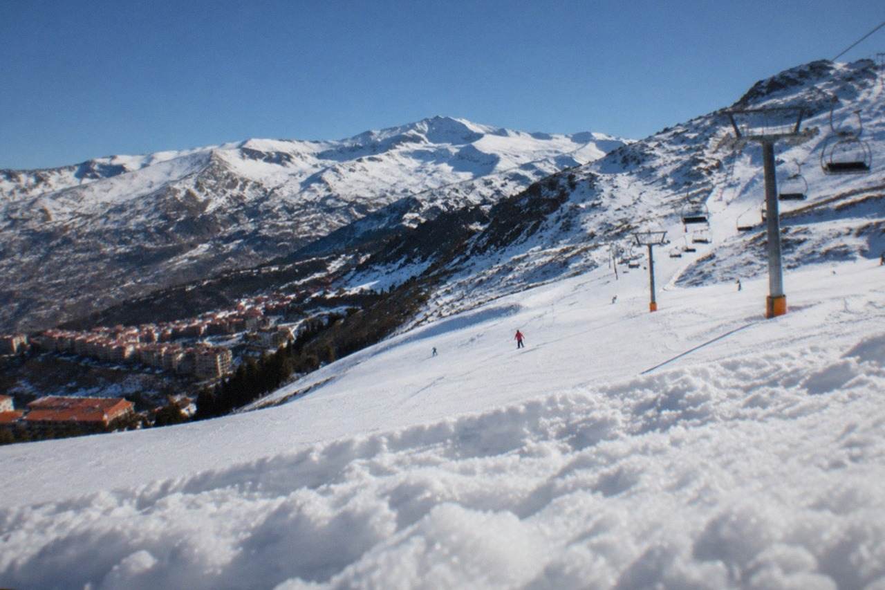 Snow-covered mountain slopes rising above red rooftops in the distance under a clear blue sky