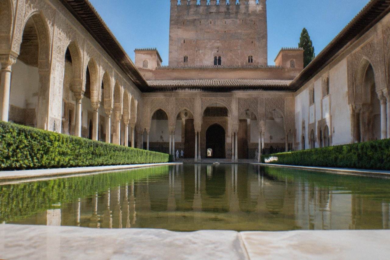 The ornate arched courtyard of the Nasrid Palaces in the Alhambra with carved stucco walls