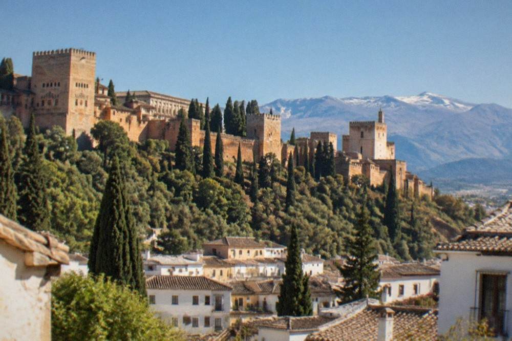 The red walls of the Alhambra seen across the city rooftops of Granada with mountains in the distance