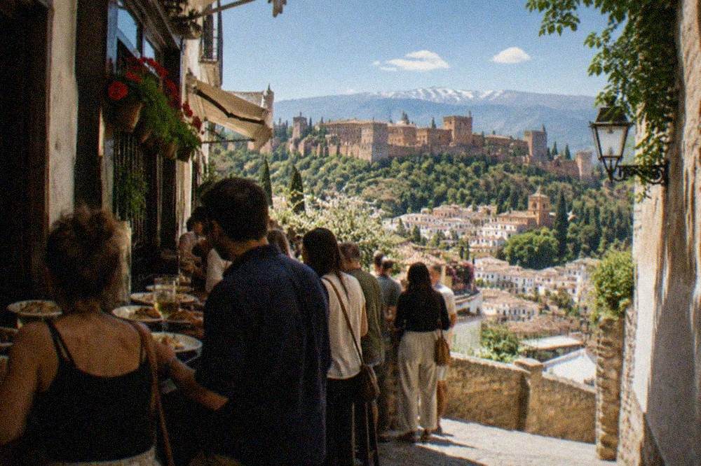 People standing at a crowded tapas bar counter with small plates and drinks in a Granada evening street