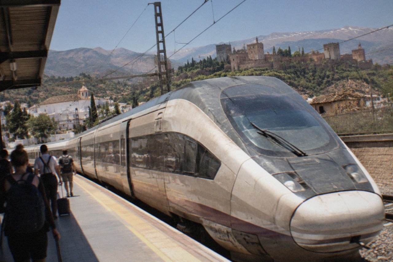 A high-speed train parked at a Spanish railway station platform with mountains in the distance