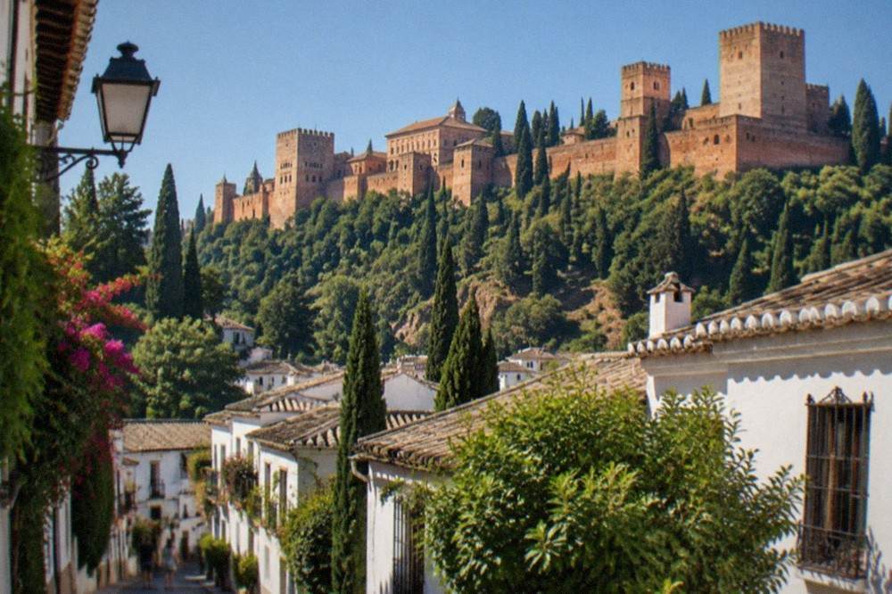 A narrow street in Granada with the Alhambra's towers visible on the hillside above the rooftops
