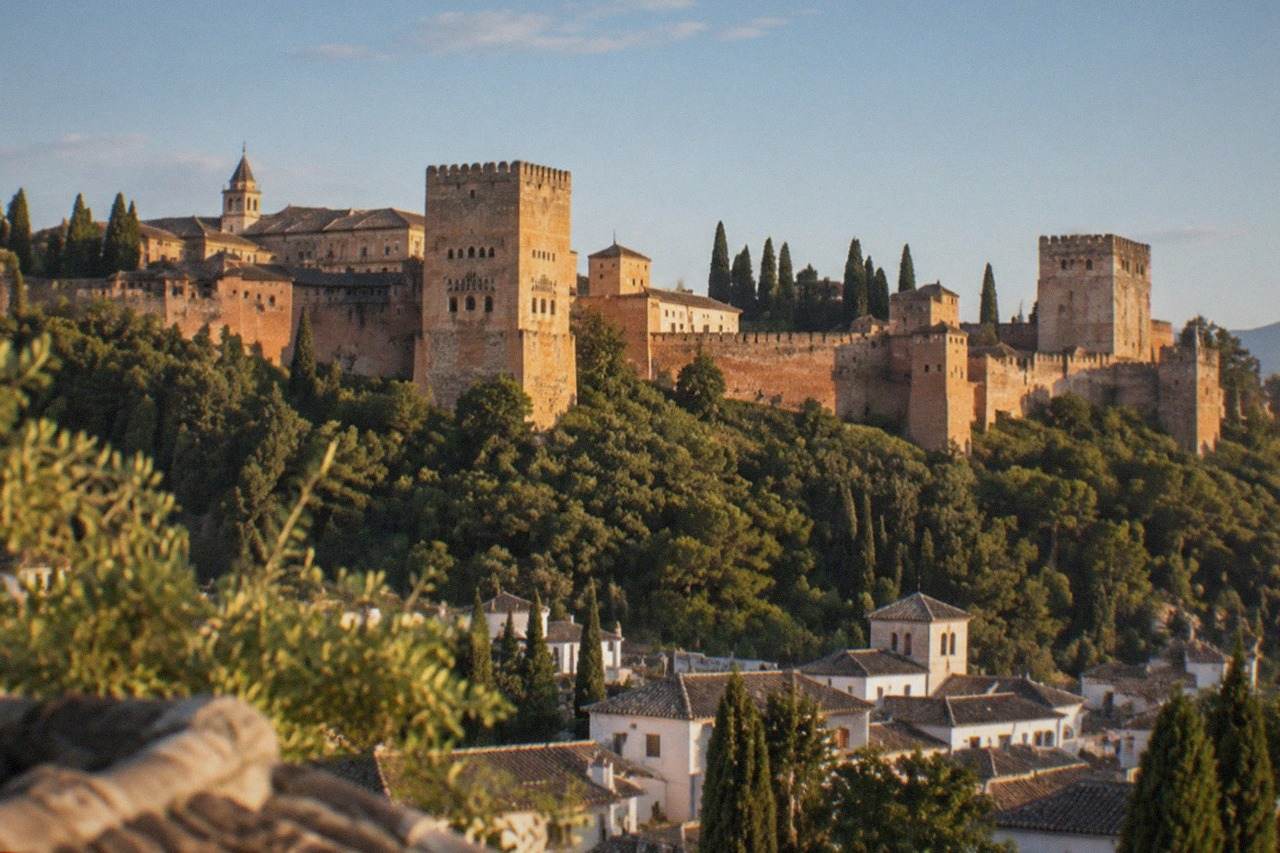 The Alhambra palace complex seen from a hillside viewpoint across the city of Granada at golden hour