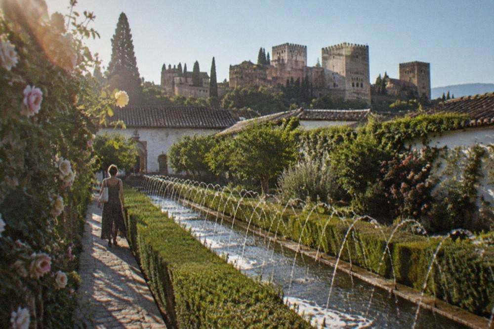 A visitor walking beside a long water channel lined with hedges in the Generalife gardens