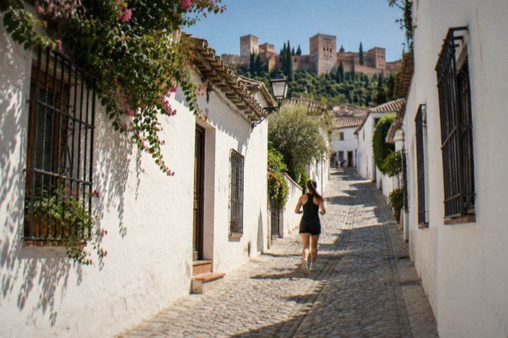 A narrow street in the Albaicin quarter with white houses and the Alhambra visible in the distance