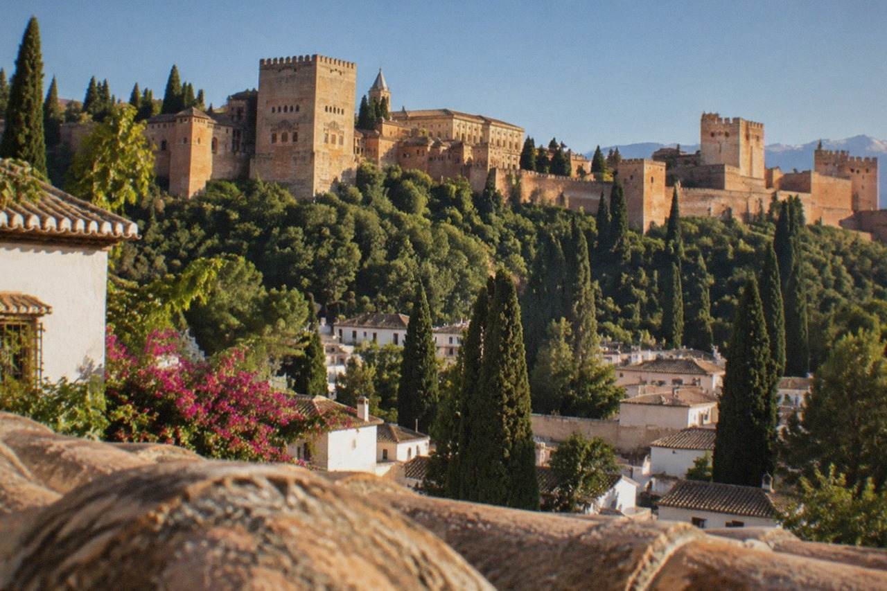 The Alhambra palace complex seen from a hillside viewpoint across the city of Granada at golden hour