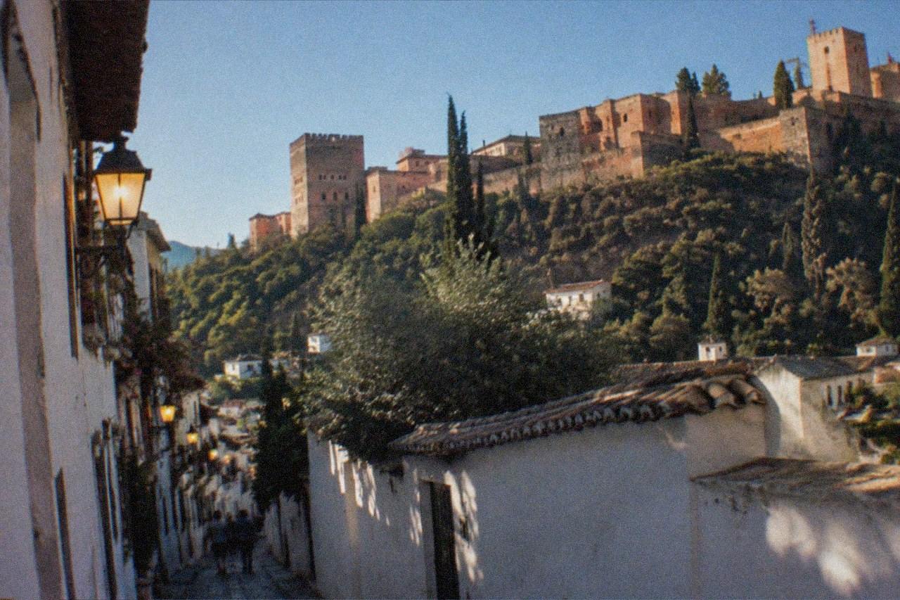 Narrow lamplit street in the Albaicin district of Granada with white houses and the illuminated Alhambra on the hill opposite
