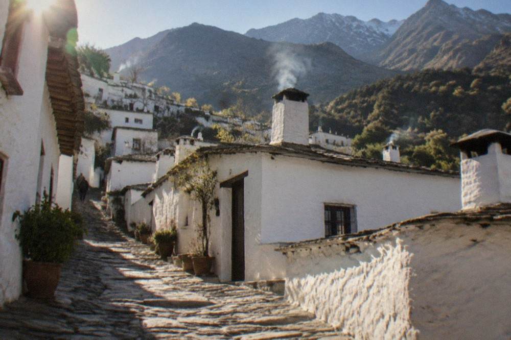 A narrow stone street between white flat-roofed houses in a mountain village