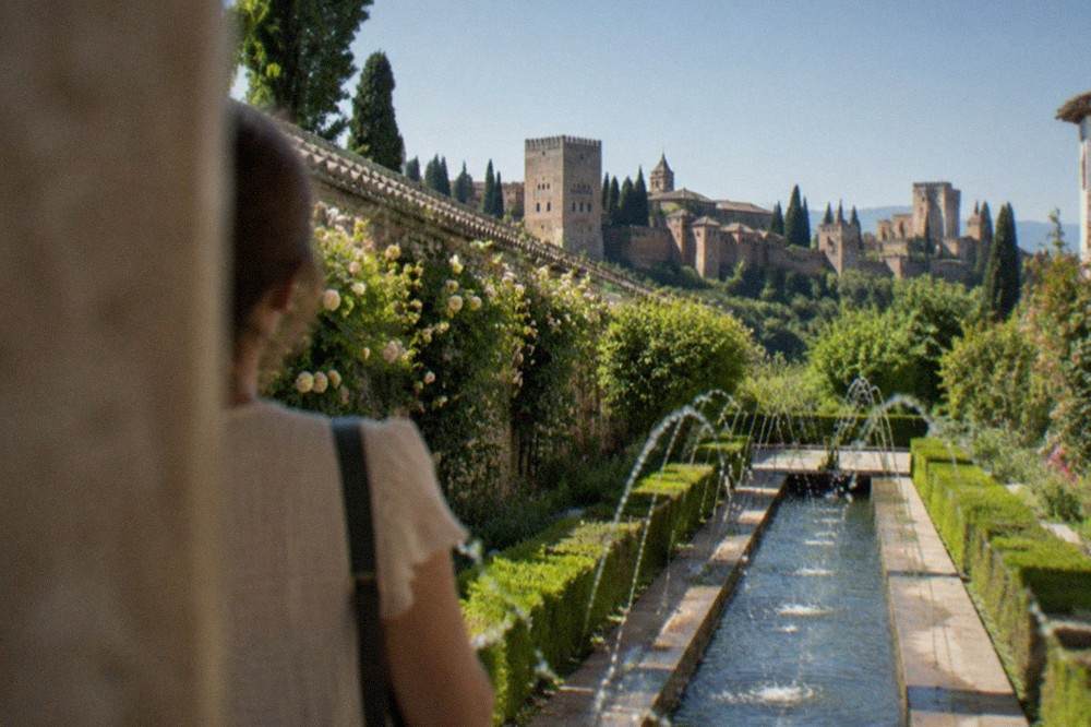 A visitor looking across at the Alhambra towers from the Generalife's upper garden viewpoint in Granada