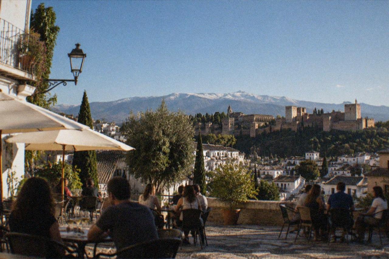 A café terrace in a Granada square with patrons chatting in the evening sun