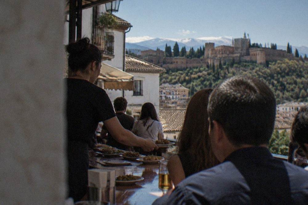 A server handing small plates of tapas across a crowded Granada bar counter