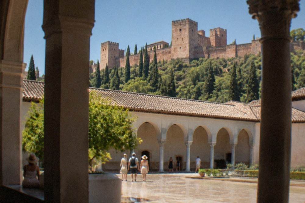 Shaded colonnade and courtyard in the Alhambra with strong midday sunlight on the far wall