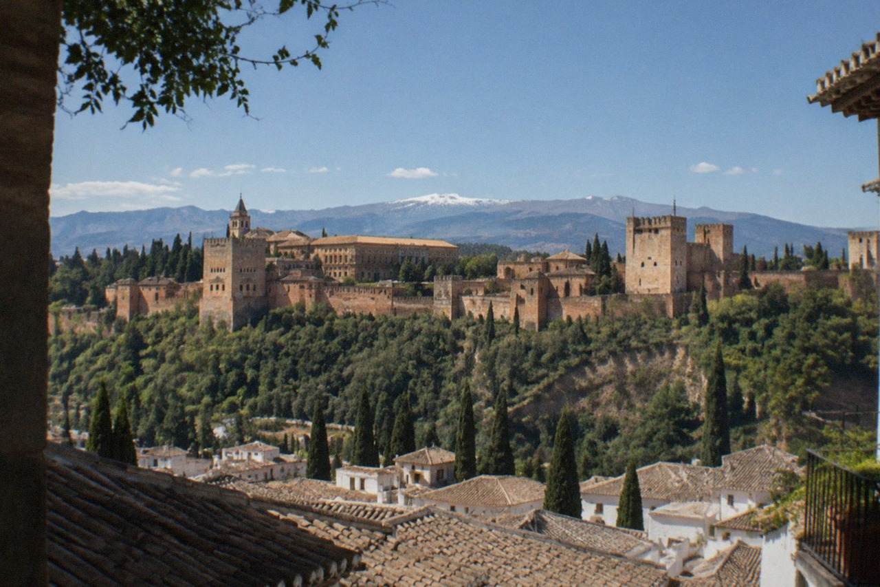 The Alhambra palace complex on its hill above the red rooftops of Granada with mountains in the distance