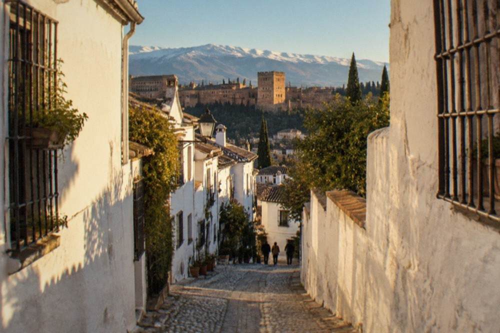 A narrow cobbled lane in the Albaicin quarter with white houses and the Sierra Nevada mountains on the horizon