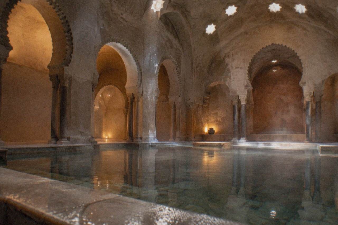 Ornately decorated Arabian bath hall with arched ceilings, warm lighting and a still marble pool