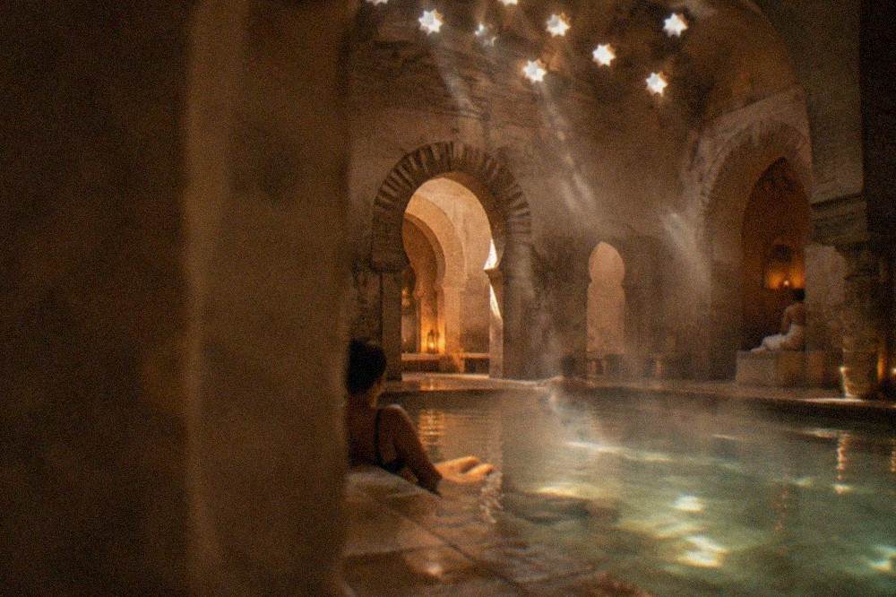 Guests relaxing beside a warm stone pool in a dimly lit Moorish-style bathhouse