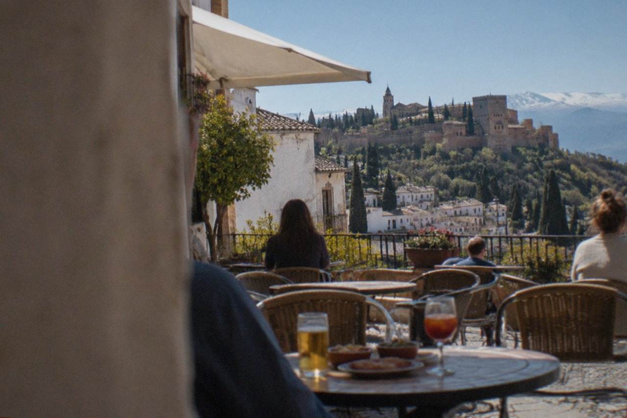 A café terrace in a Granada square with small tapas plates and drinks on the tables