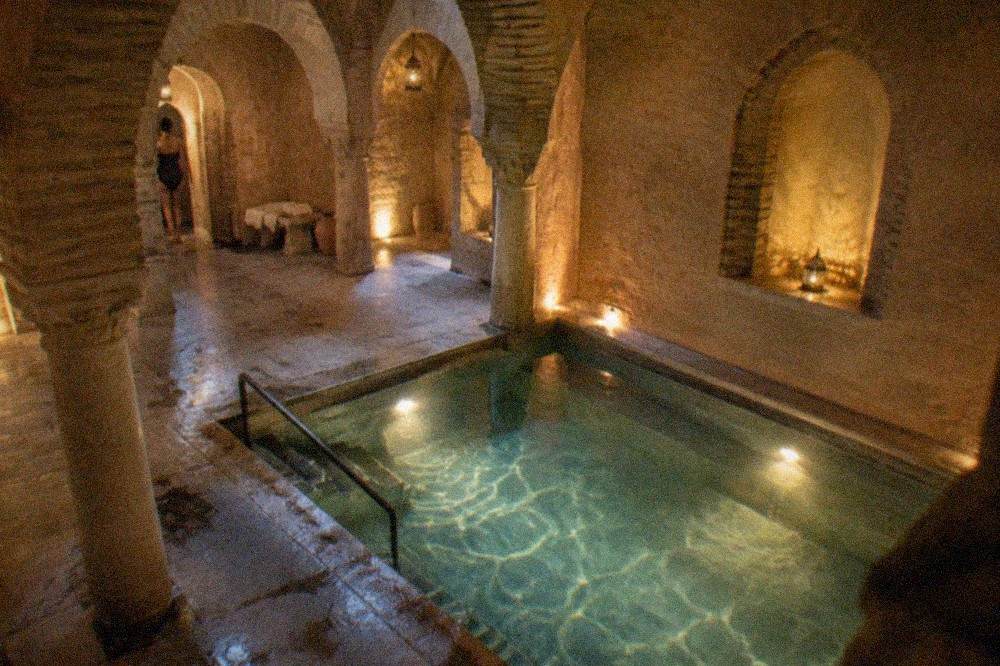 A traditional Granada hammam interior with warm stone walls, arches and a lit plunge pool
