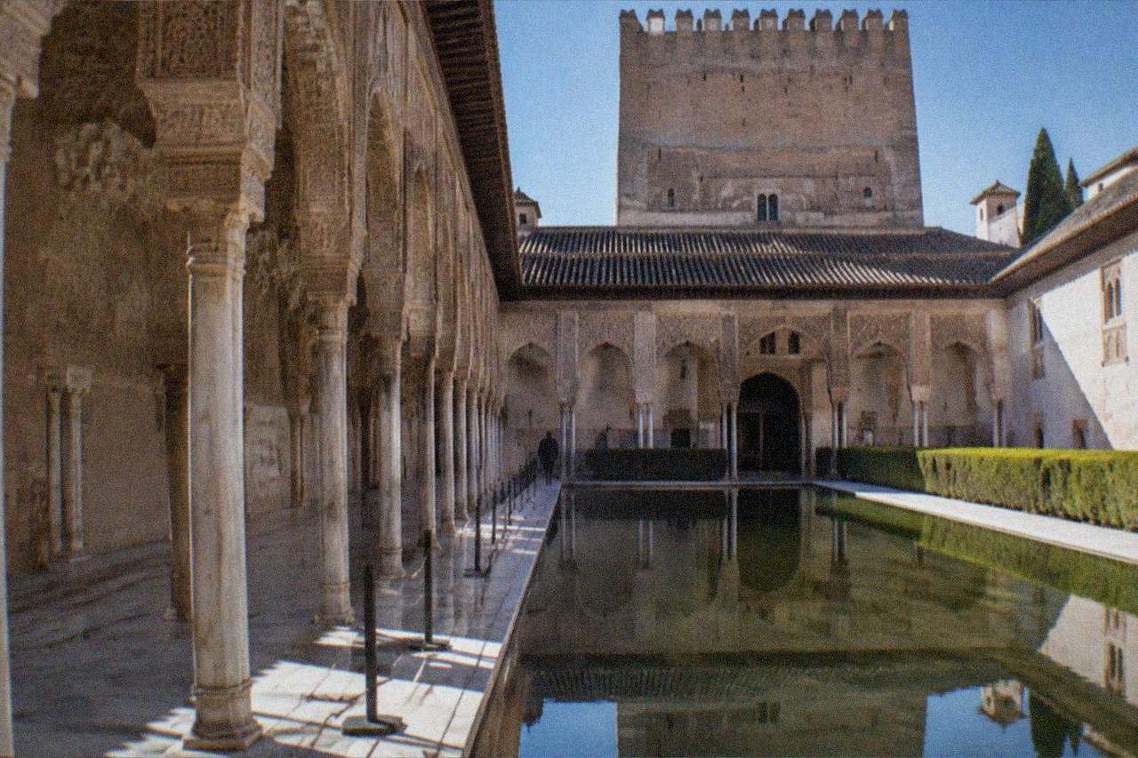 The Nasrid Palaces of the Alhambra lit by warm floodlights against a dark evening sky in Granada