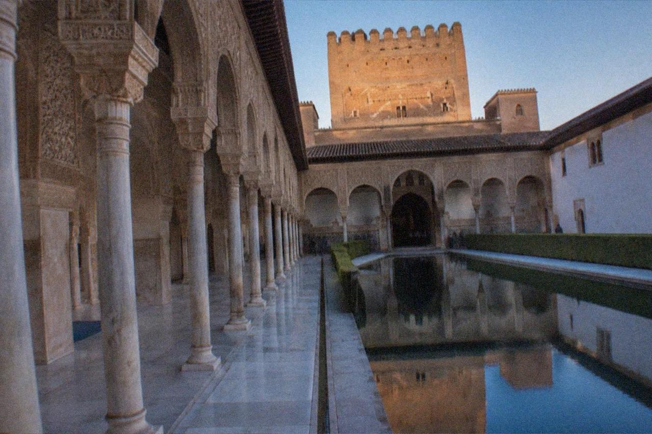 The ornate arched courtyard of the Alhambra's Nasrid Palaces under an afternoon sky