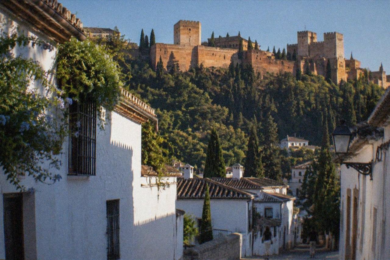 Narrow street with white houses in the Albaicin district of Granada with the Alhambra on the hillside above