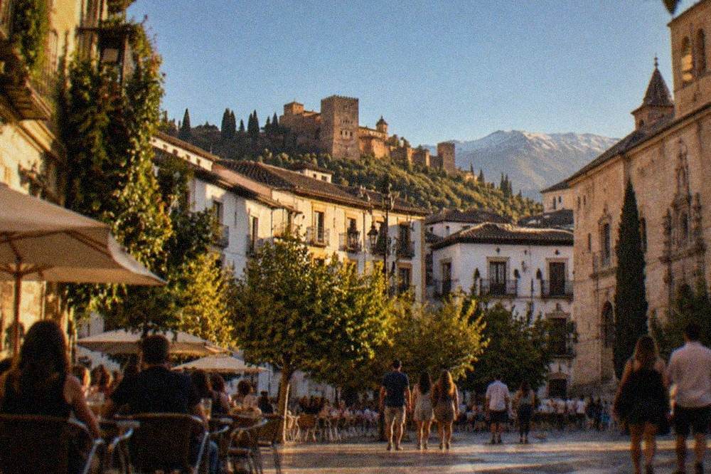 Evening crowds on a tiled plaza in central Granada with outdoor tables and historic facades