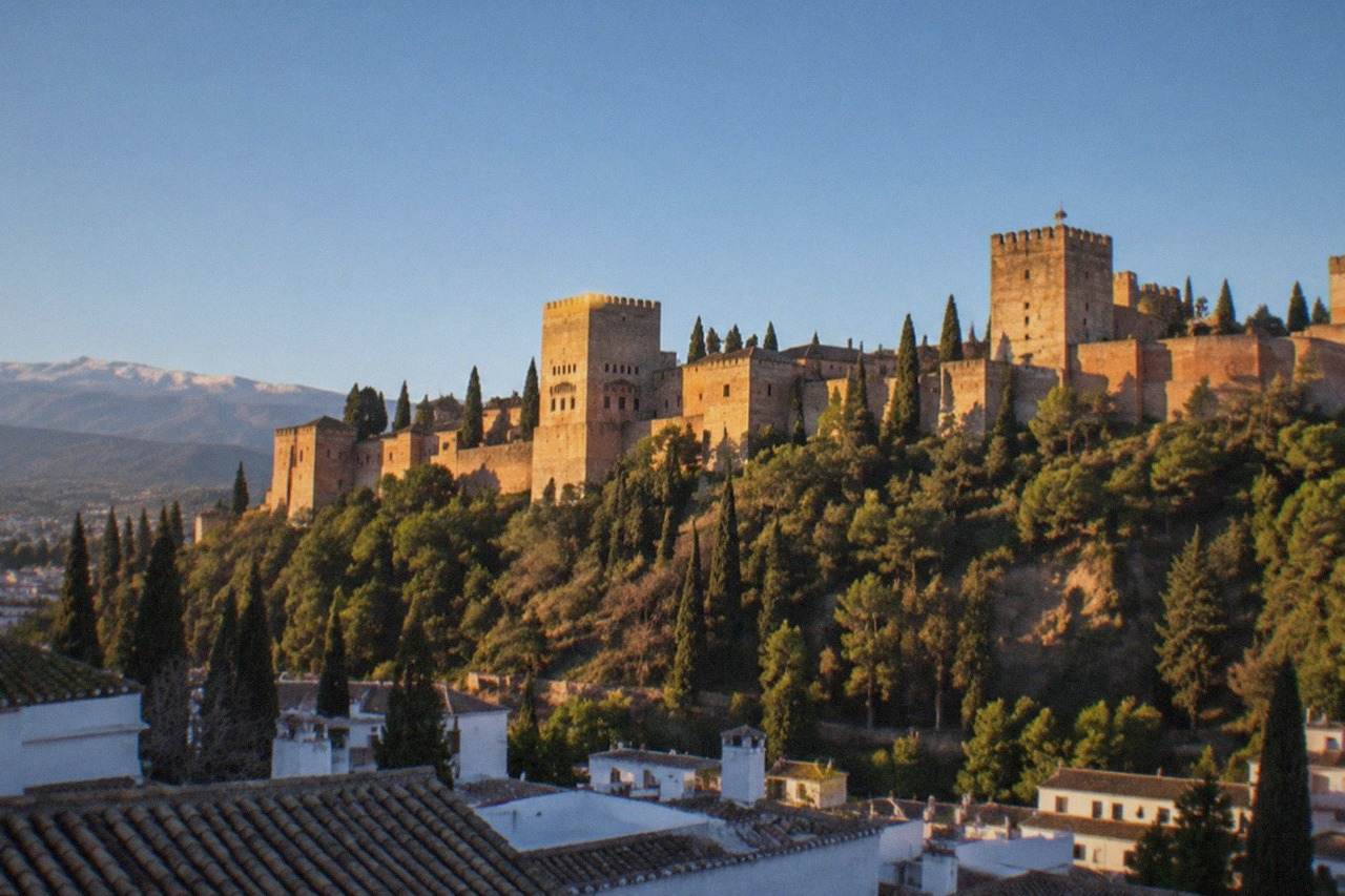 The reddish stone walls and towers of the Alhambra fortress overlooking the city of Granada at golden hour