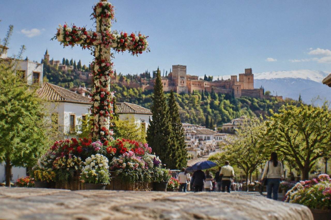 A decorated street cross covered in flowers standing in a Granada plaza during a spring festival