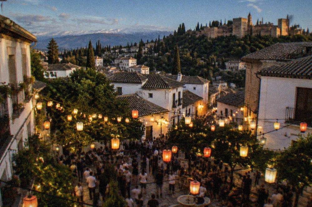 Crowds gathered in an Andalusian plaza at night during a festival with lanterns strung between buildings