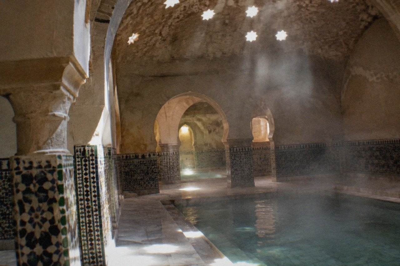Ornately tiled Arabian-style bathhouse interior with arches, marble floors and softly lit pools