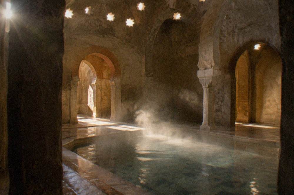 Steam rising softly from a warm marble plunge pool in a dimly lit bathhouse room