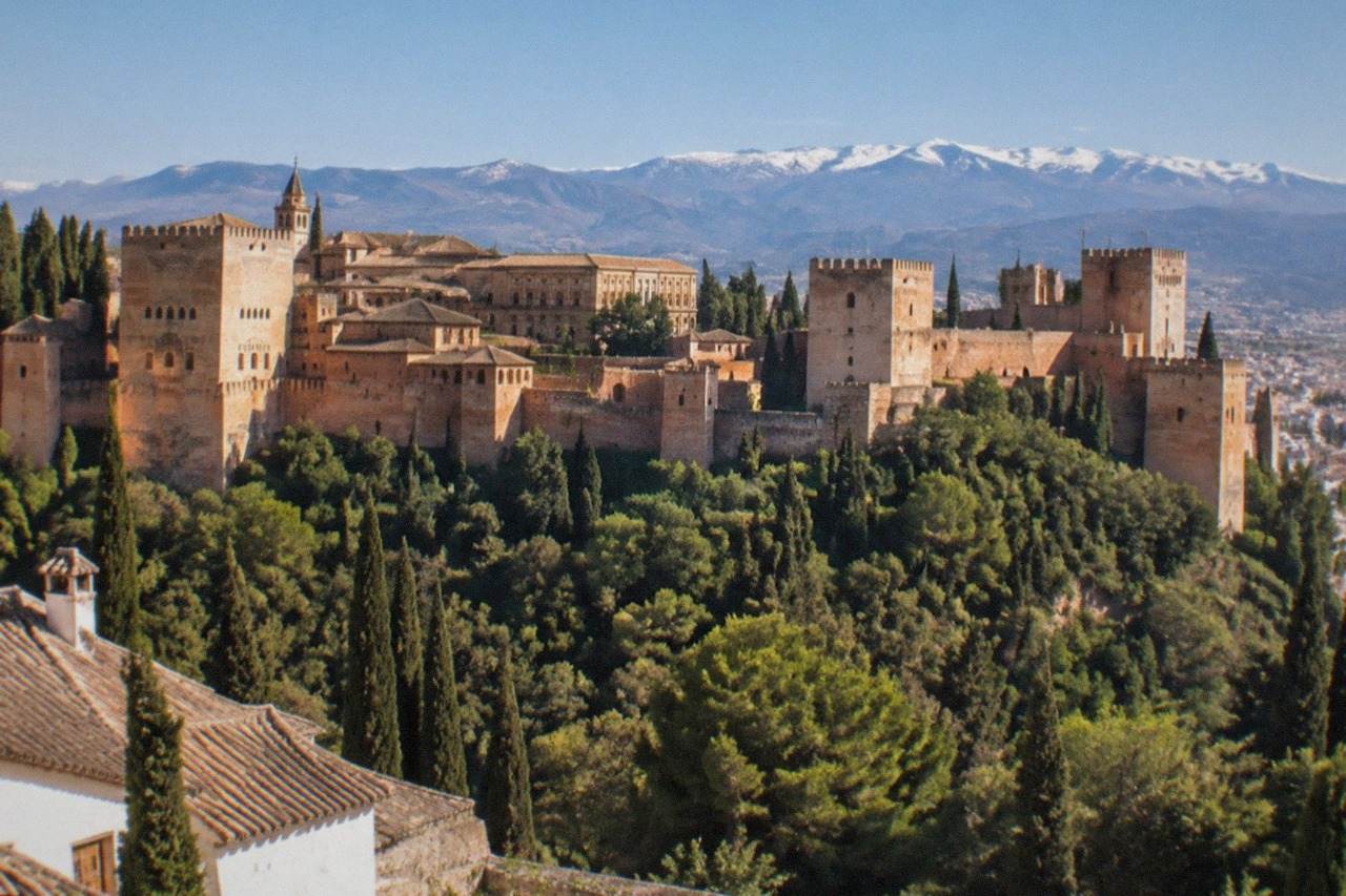 The Alhambra palace complex seen across Granada under a clear sky, with the Sierra Nevada mountains on the horizon