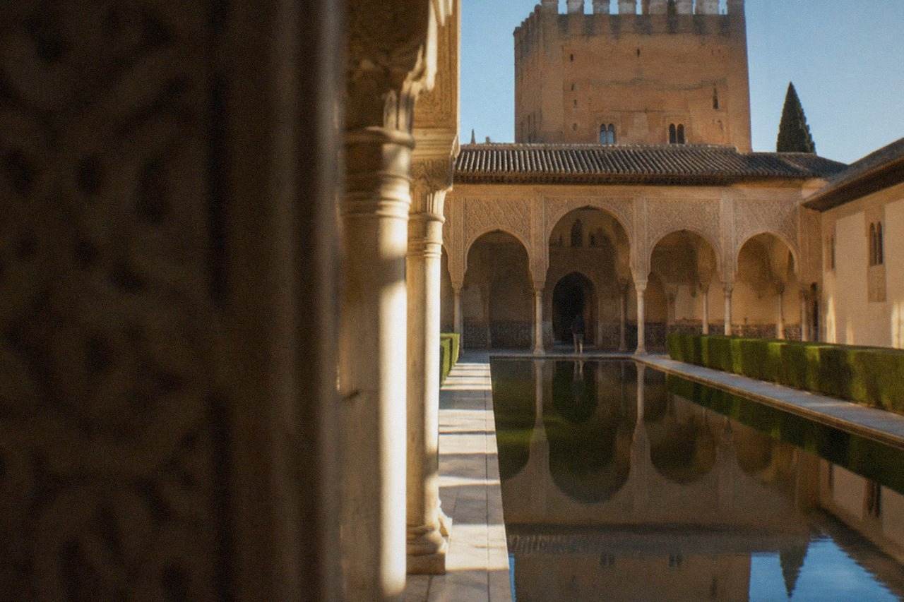 The Nasrid Palaces courtyard at the Alhambra with ornate arches and a reflecting pool in warm morning light