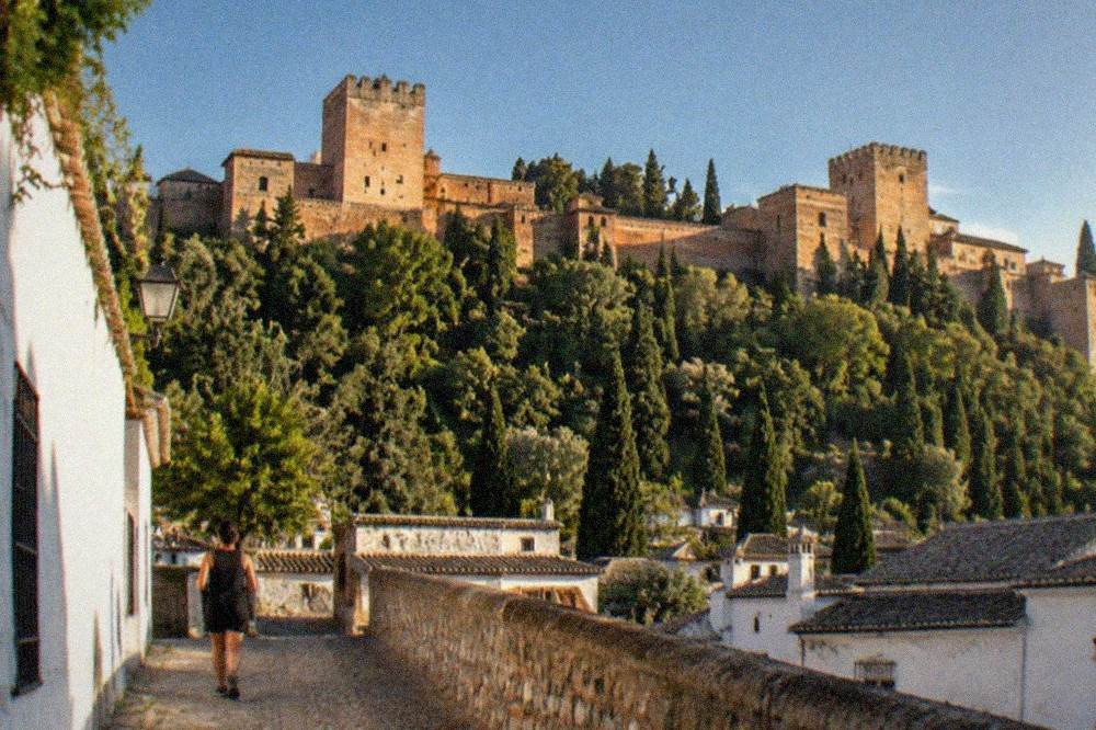 The Alhambra palace walls and towers lit at night above the dark rooftops of Granada