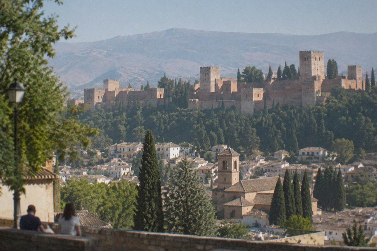 View across Granada from a hillside square with the Alhambra and mountains behind the city