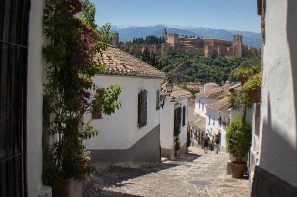 Narrow cobbled street with white houses climbing toward a hilltop square in the Albaicin