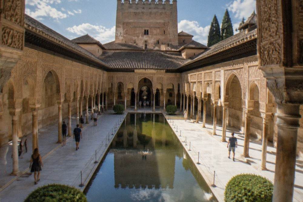 Visitors walking through the columned Court of the Lions at the Alhambra on a bright day