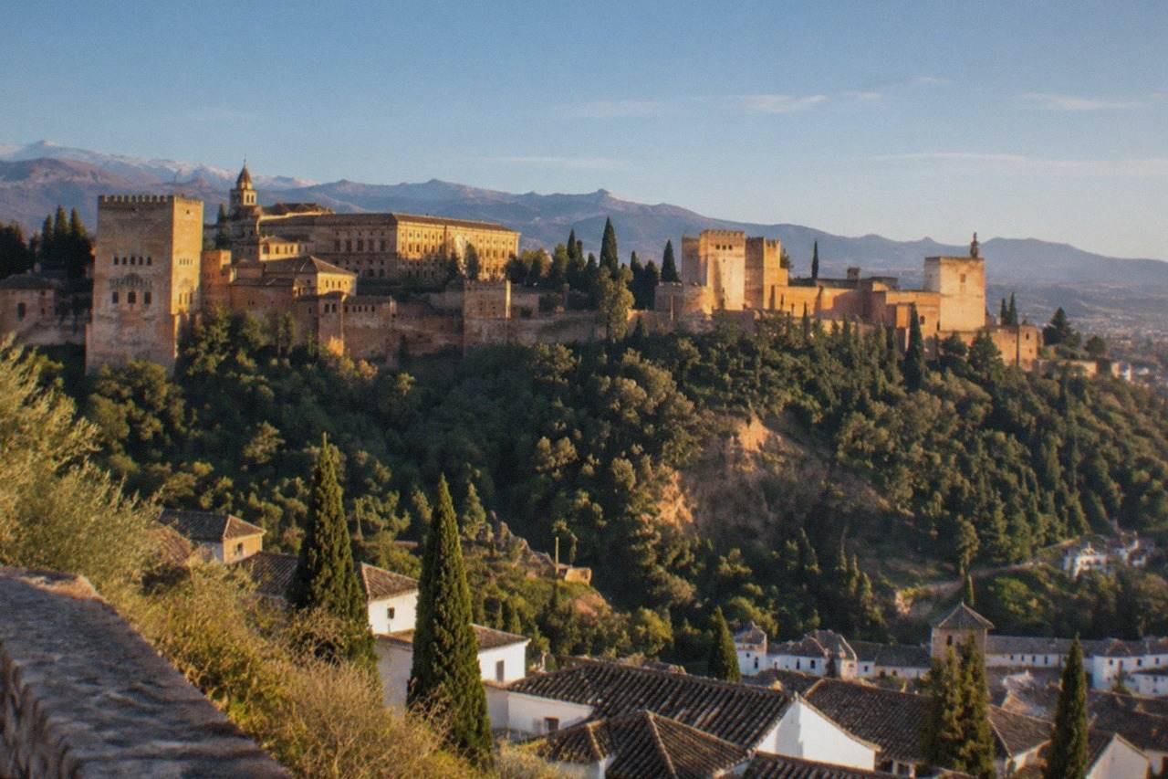 The Alhambra palace complex seen across a valley from a hillside viewpoint at golden hour