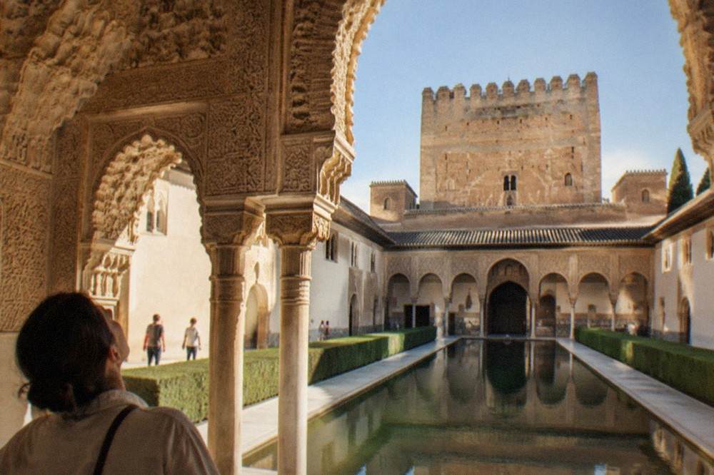 A visitor looking up at the ornate vaulted ceiling of a hall in the Nasrid Palaces