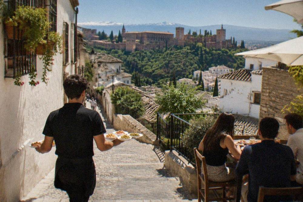 A waiter carrying small plates of tapas to an outdoor table in a narrow Granada street