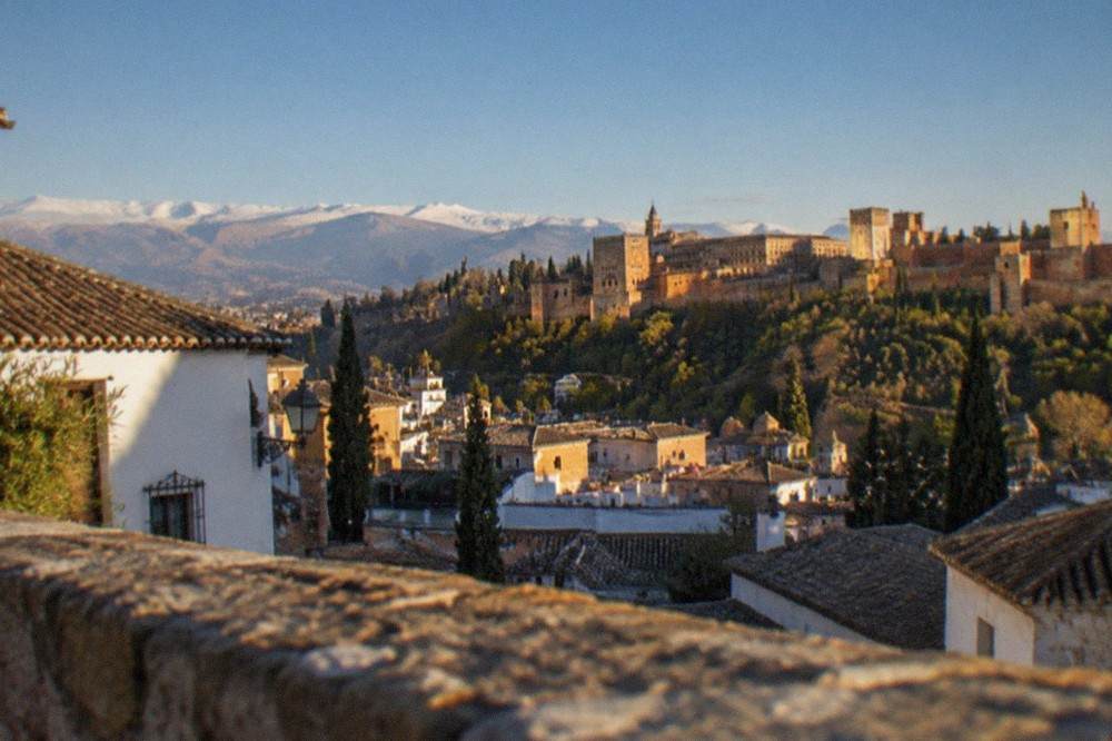 View across Granada rooftops toward the Alhambra on its wooded hill at golden hour
