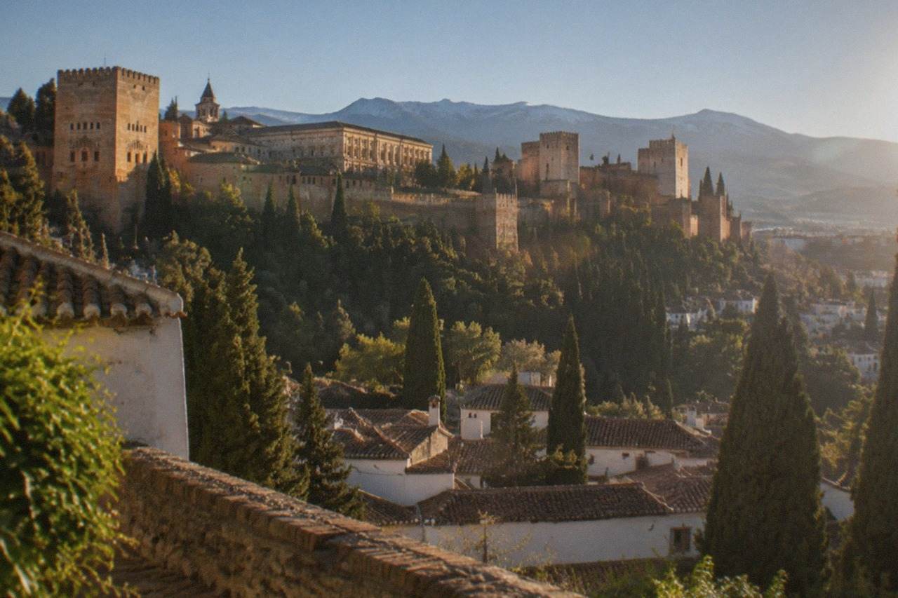 The Alhambra palace complex on its hill above the red roofs of Granada with mountains in the distance