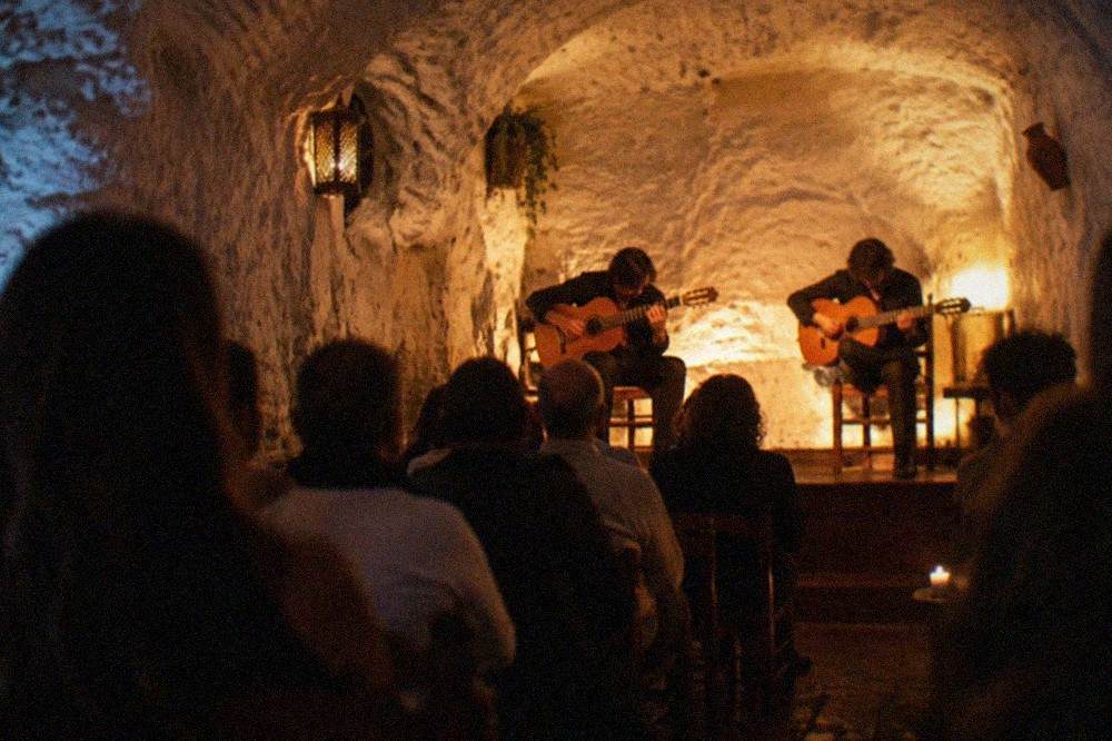 An audience seated in a dimly lit cave watching musicians play flamenco guitar during a show
